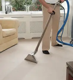 Professional carpet cleaner using a hot-water extraction wand and hose machine in a living room in Oakland, CA.