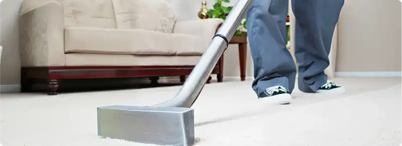 Carpet cleaning technician using a hot-water extraction wand on a light-colored carpet in a living room, Oakland, CA.