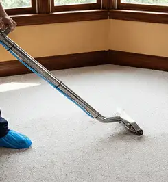 Steam carpet cleaning technician using a hot-water extraction wand on a residential carpet, wearing blue protective shoe covers Oakland, CA.