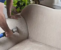 Professional upholstery cleaner deep-cleaning a fabric sofa with a handheld extraction tool and hose in Oakland, CA.
